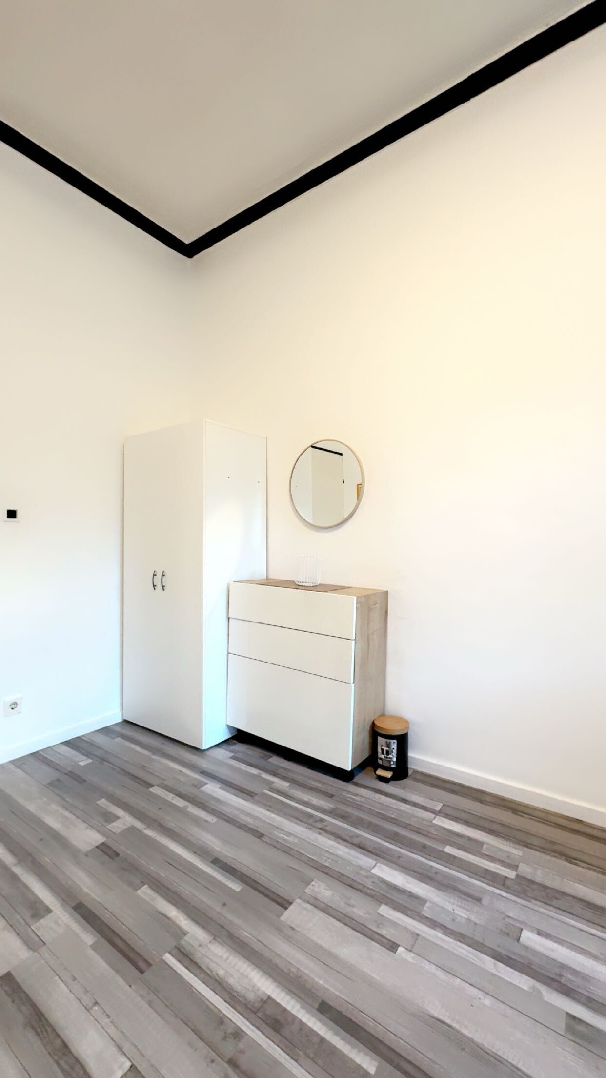 Ein Zimmer mit einem weißen Wandschrank, einem runden Spiegel und einer kleinen Mülltonne.