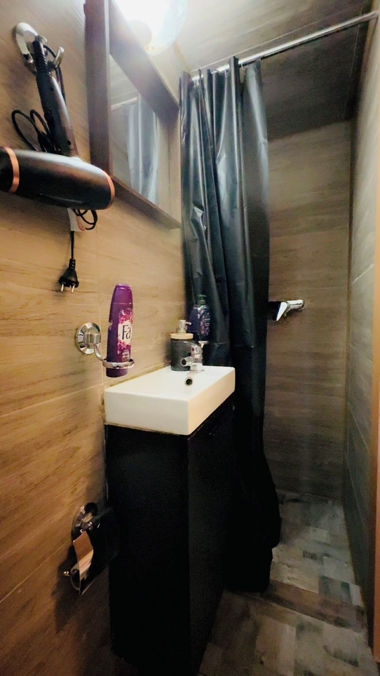 Un baño pequeño con lavamanos, espejo, secador de pelo y cortina de ducha.