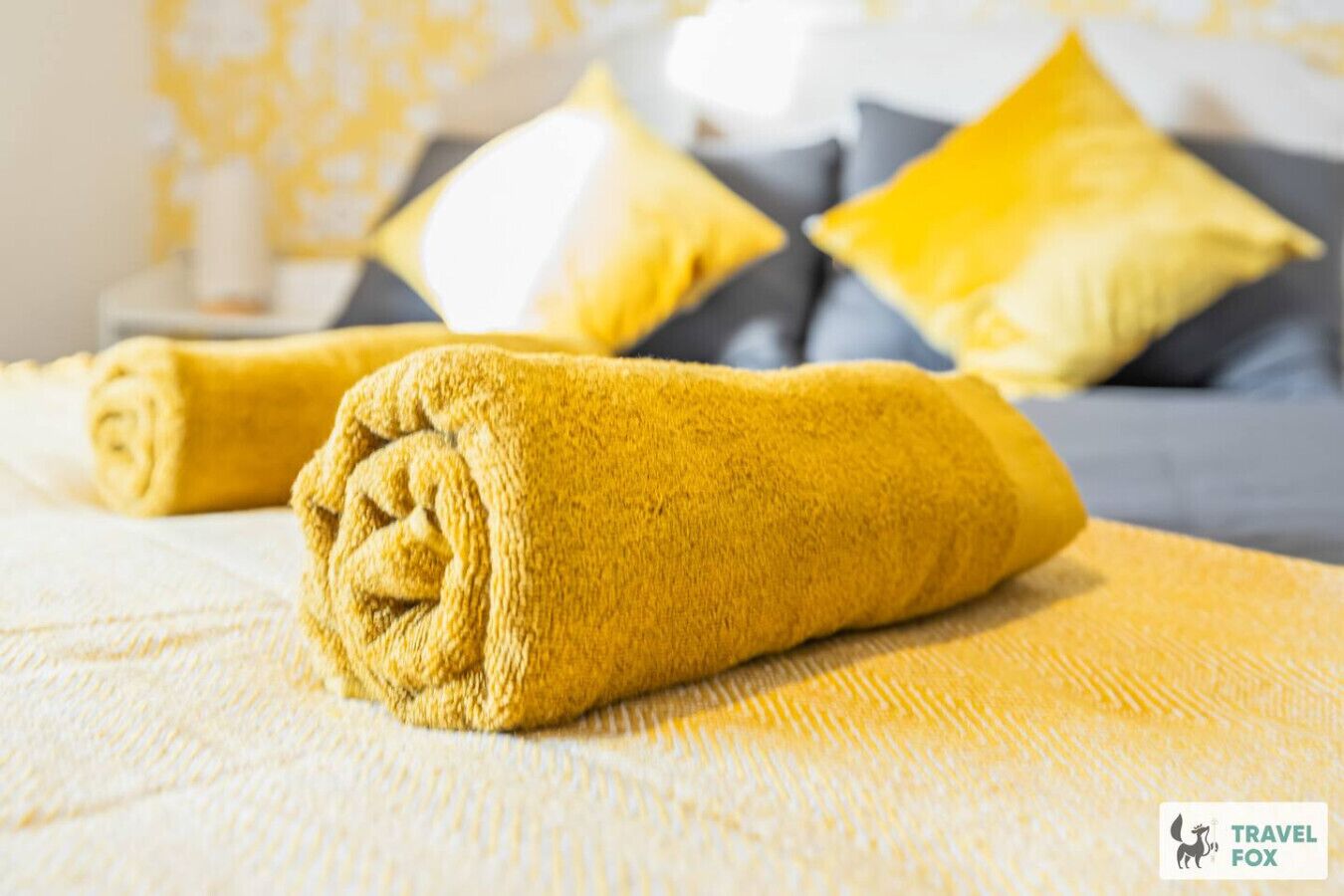 En snyggt bäddad säng med en gul handduk, en grå soffa och matchande kuddar i ett hotellrum.