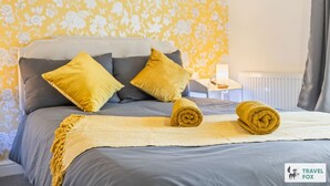 A neatly made bed with a grey bedspread, two yellow pillows, and a rolled towel on the bed. - Cheadle Cottage - Hot Tub and Pool Table! (Alton Towers & Staffordshire Villages)