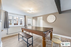 Ein geräumiges Zimmer mit einem Holztisch, einer Bank und einer Uhr an der Wand.