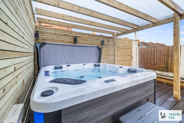 Ein Whirlpool in einem überdachten Holzdeck-Bereich mit einer Pergola.