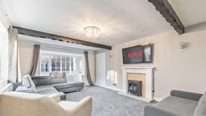 A living room with a fireplace, a television mounted above it, and a sofa. - Cheadle Cottage - Hot Tub and Pool Table! (Alton Towers & Staffordshire Villages)