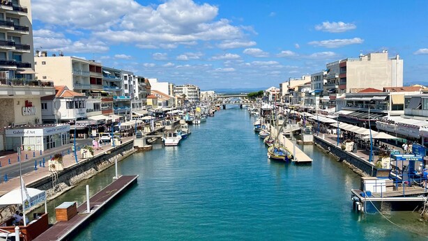 A marina with boats docked along a canal, surrounded by buildings and shops. - Dream house ground floor on the beach: prime location at the Mediterranean Sea (Palavas-les-Flots)