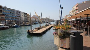 A marina with boats docked, a pedestrian walkway, and buildings with balconies. - Dream house ground floor on the beach: prime location at the Mediterranean Sea (Palavas-les-Flots)