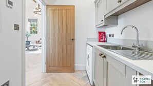 A modern kitchen with a wooden door, built-in appliances, and a countertop with a sink. - The Old Chapel - Lower Peaks (Alton Towers & Staffordshire Villages)