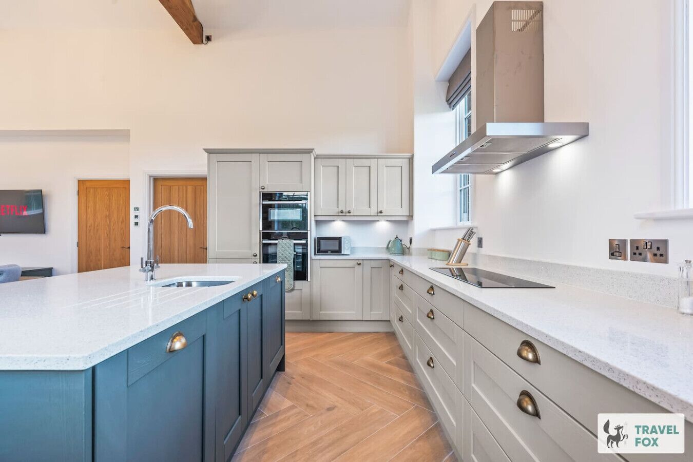 A modern kitchen with a central island, built-in oven, microwave, and stainless steel range hood.