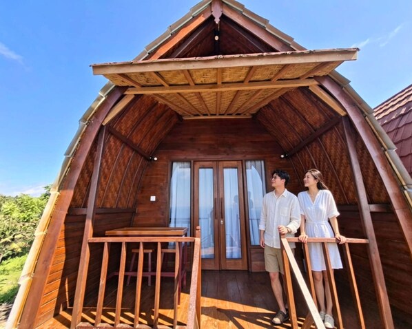 A wooden cabin with a balcony, a wooden table, and a view of the surrounding greenery. - Sea Cliff Eco Nusa Penida (Penida Island)