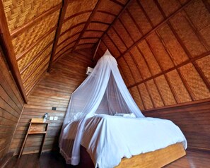 A wooden room with a bed, a small wooden table, and a mosquito net. - Sea Cliff Eco Nusa Penida (Penida Island)