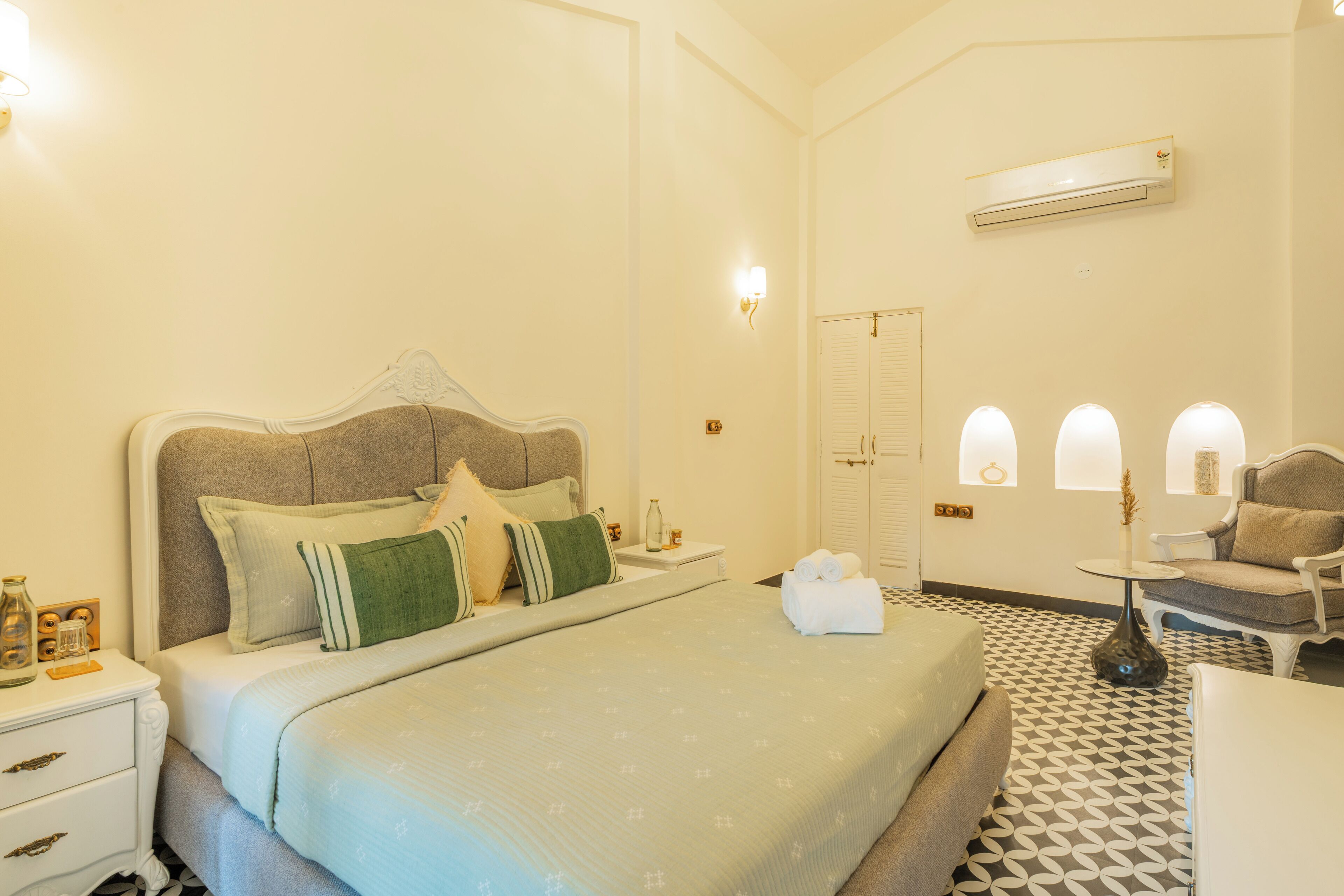 A hotel room with a bed, bedside table, lamp, chair, and a patterned floor.