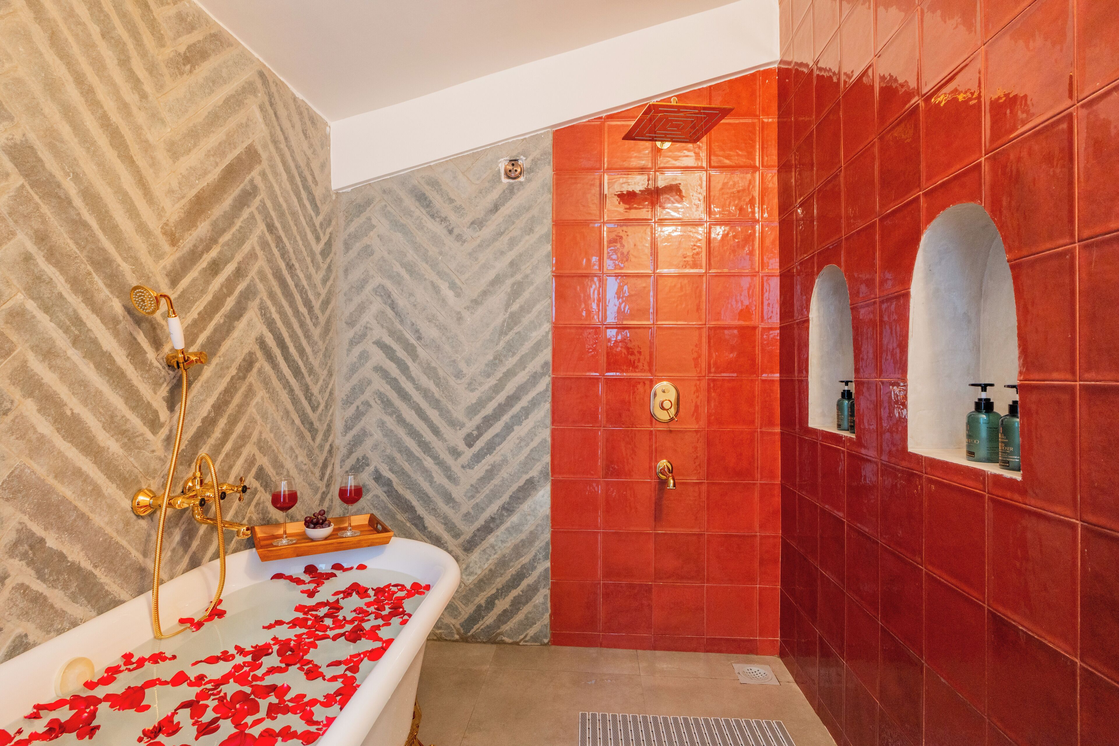 Un baño con una bañera independiente, una ducha con grifo dorado y paredes de azulejos rojos.
