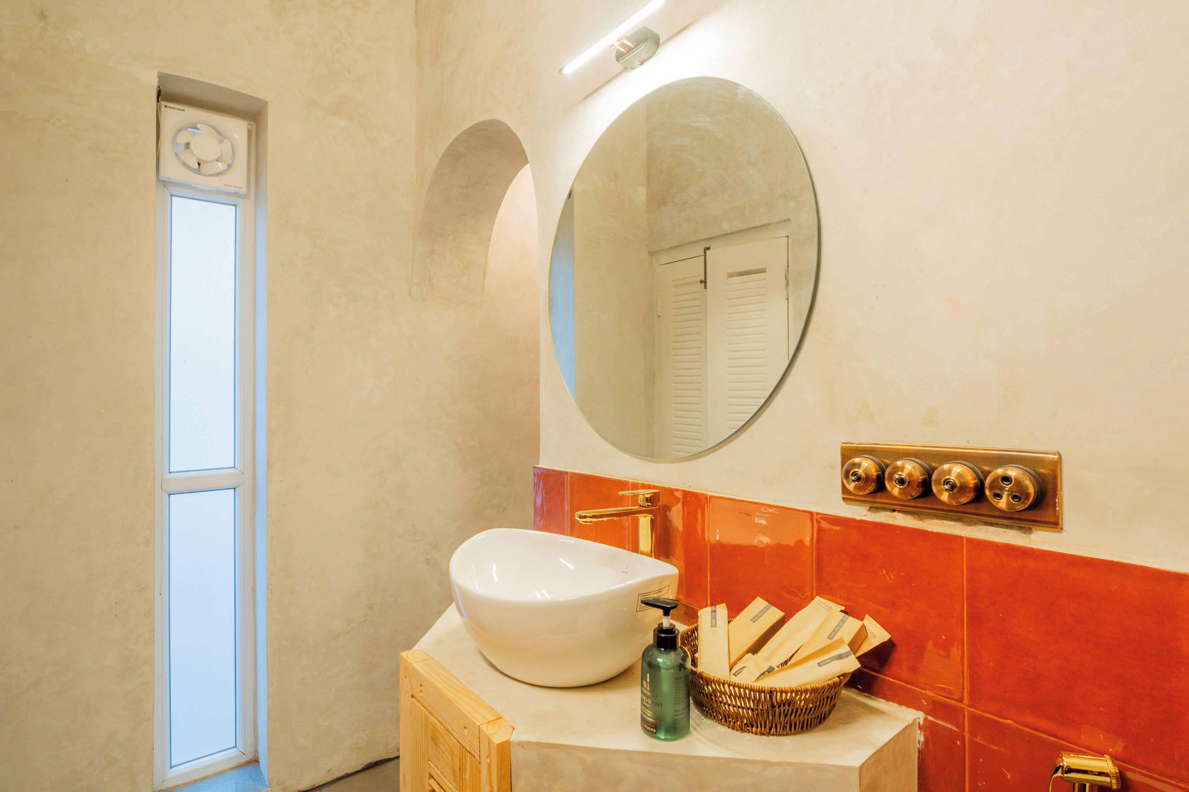 Een badkamer met een wit wastafel, een spiegel, een raam en een betegelde muur.