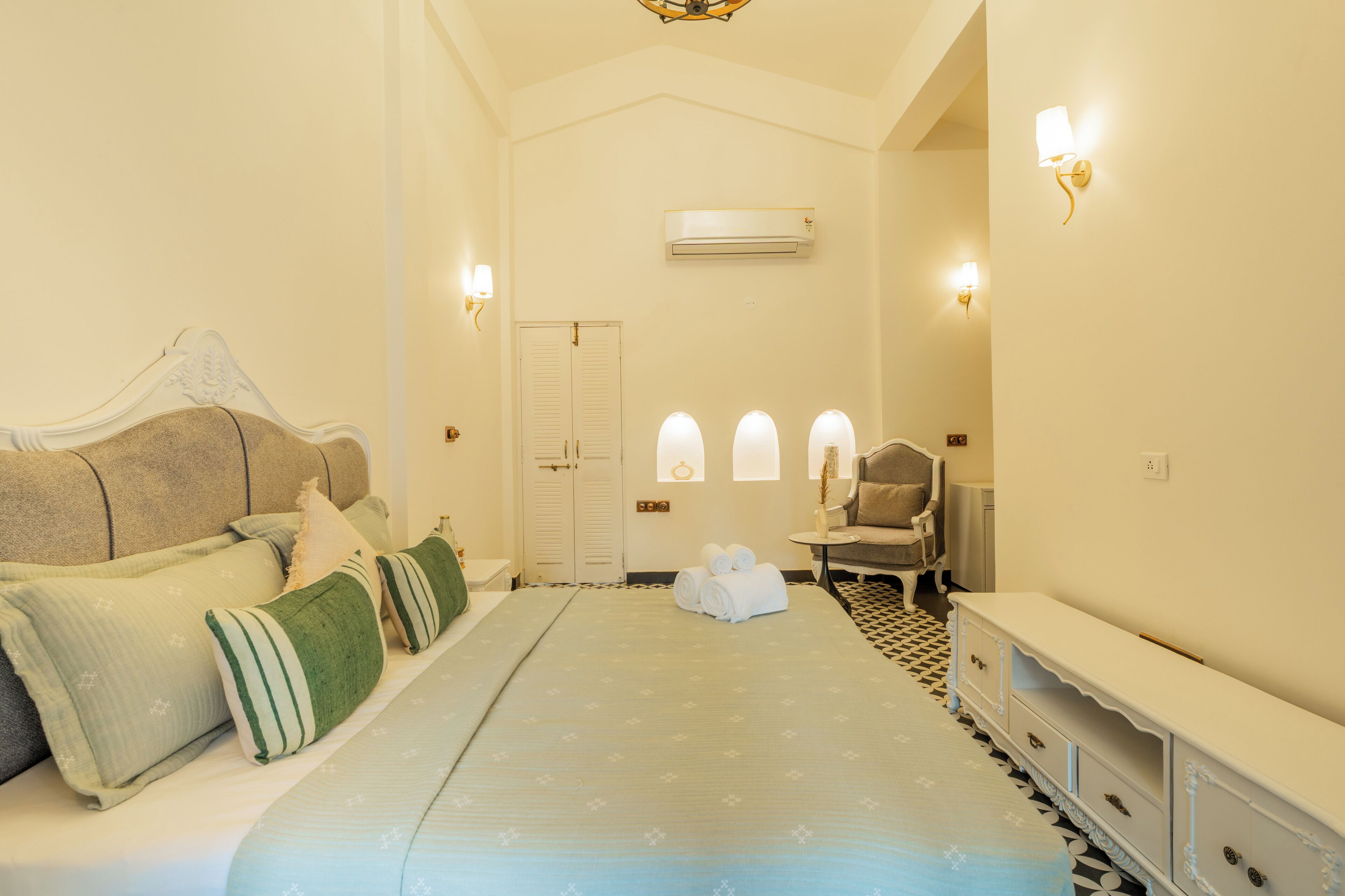 A hotel room with a bed, a chair, a dresser, and an air conditioning unit.