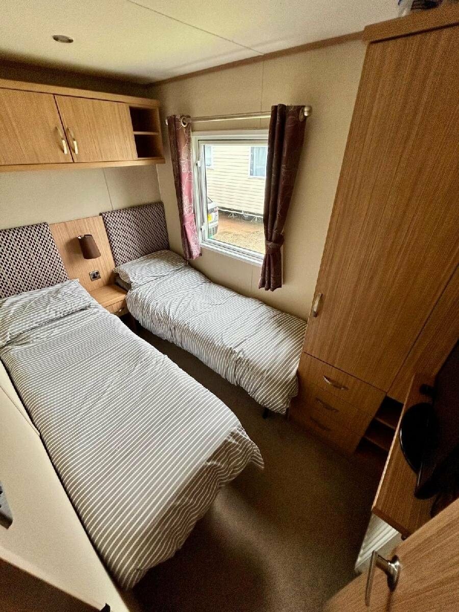 A compact RV bedroom with two beds, a window with curtains, and a wardrobe.