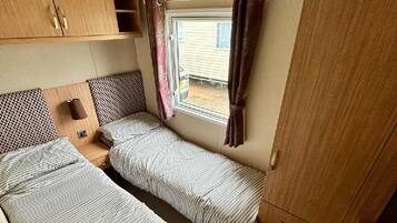 A compact RV bedroom with two beds, a window with curtains, and a wardrobe.