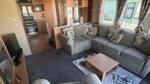 Ein gemütlicher, kompakter Wohnraum mit einer Sofagarnitur, einem Couchtisch und einer Küchenzeile mit Schränken und einem Herd.