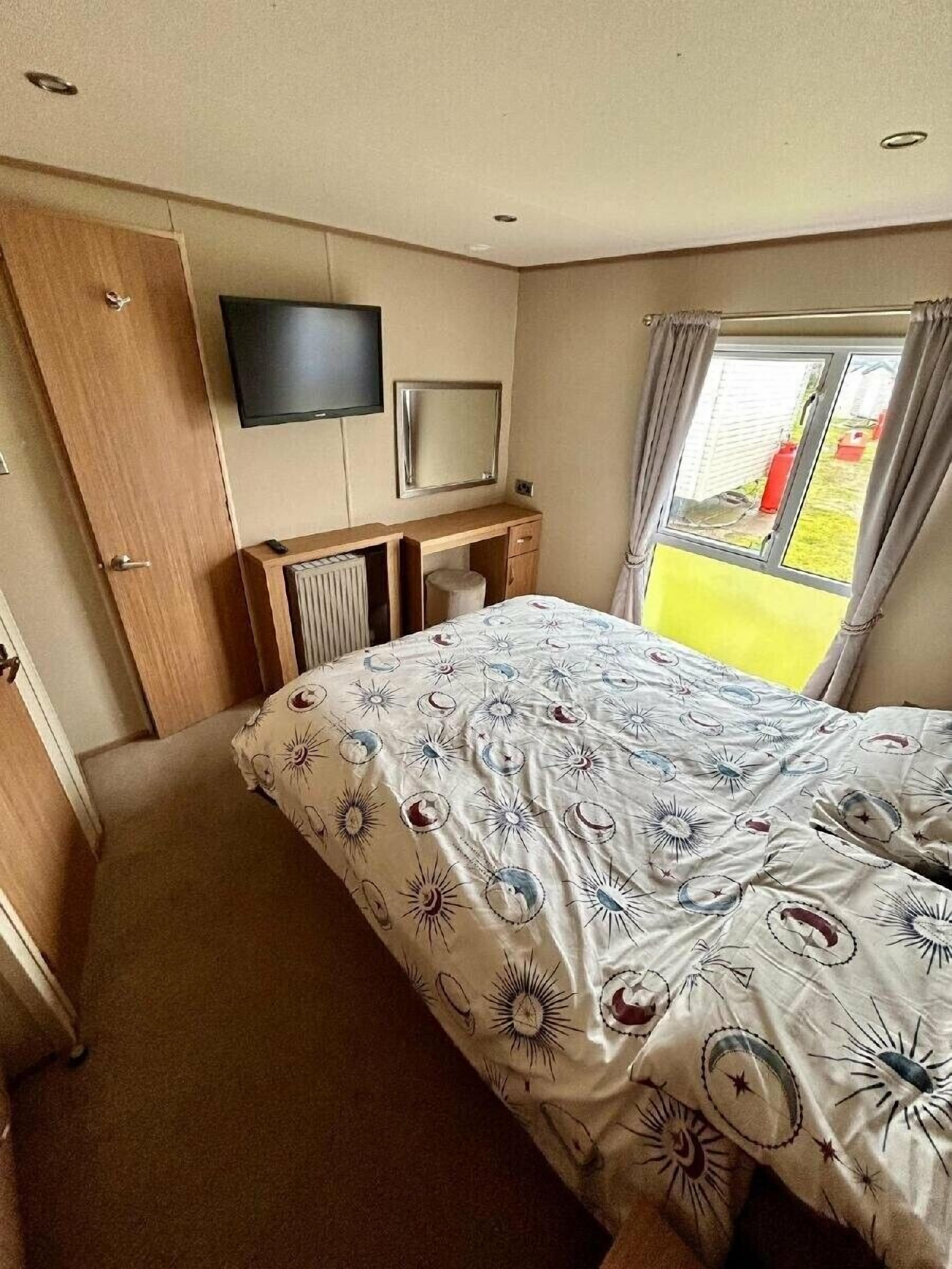 A bedroom with a bed, a desk, a television, and a window with curtains.