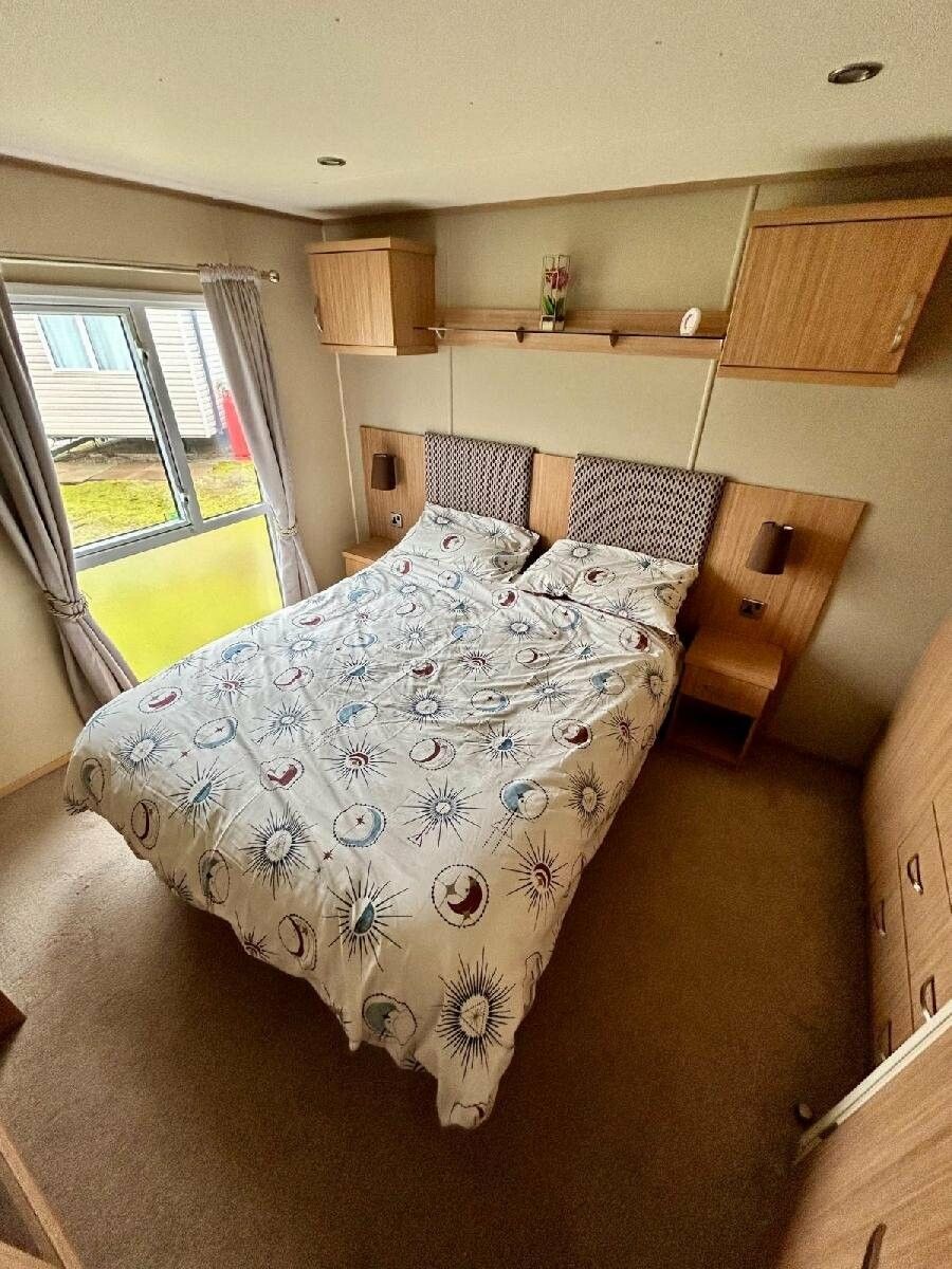 A compact bedroom with a bed, a small bedside table, a nightstand, and a window with curtains.