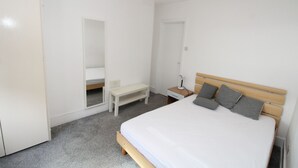 A bedroom with a single bed, a bedside table with a lamp, a small desk, and a mirror. - Commuter’s Dream: 5 Mins from Clapham Jct Station (London)