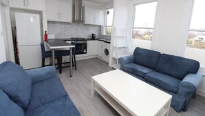 A compact living space with a kitchenette, a sofa, a dining table, and a washing machine. - Commuter’s Dream: 5 Mins from Clapham Jct Station (London)