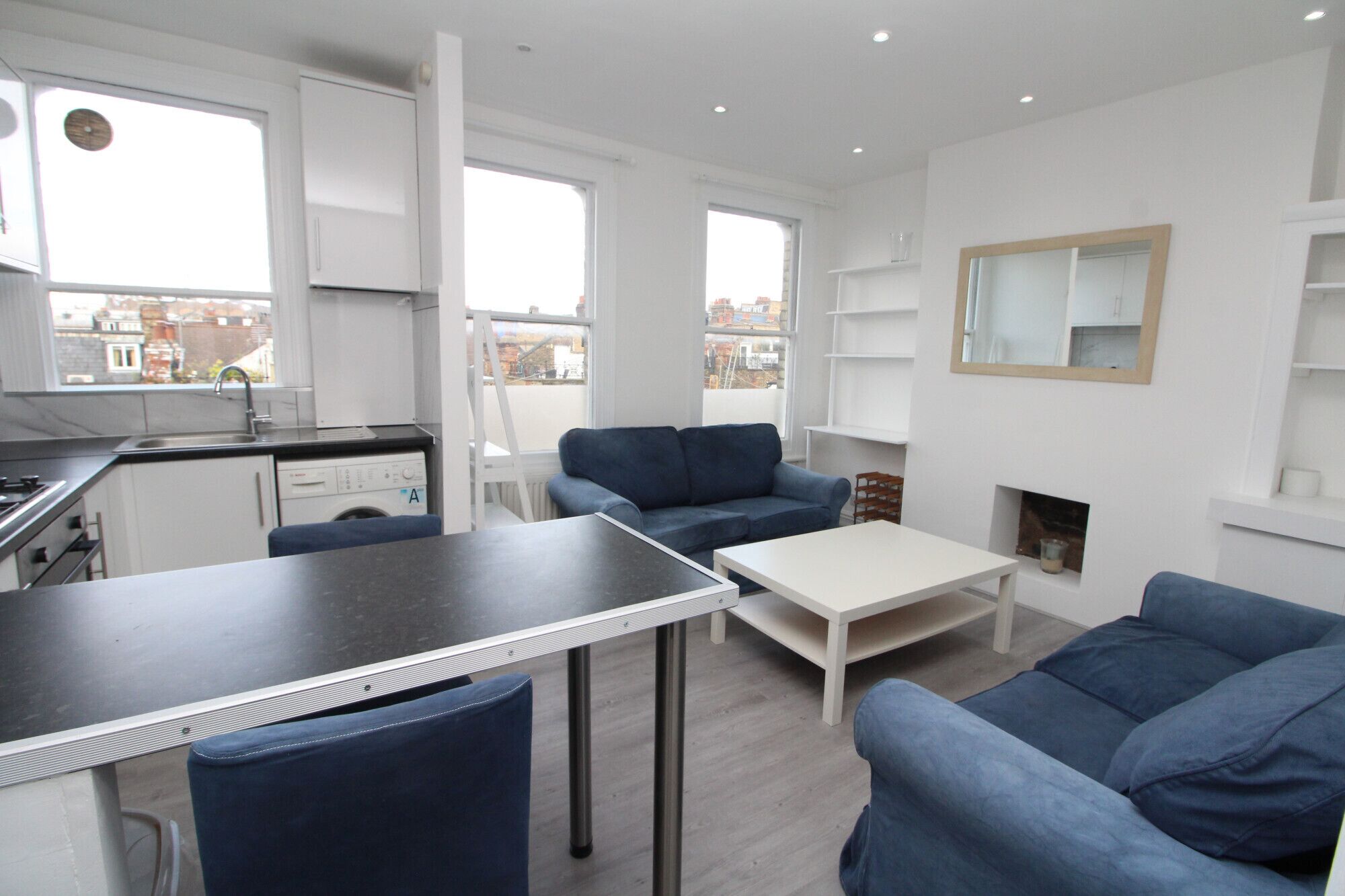 Un appartement moderne comprenant une cuisine, un coin repas et un salon. Il dispose d’une grande fenêtre, d’une cheminée et offre une vue sur la ville.