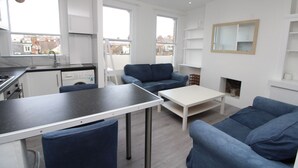 A modern apartment with a kitchen, dining area, and living room. It features a large window, a fireplace, and a city view. - Commuter’s Dream: 5 Mins from Clapham Jct Station (London)