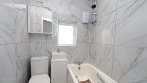 A bathroom with a toilet, sink, and bathtub against marble walls. - Commuter’s Dream: 5 Mins from Clapham Jct Station (London)