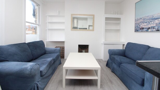 A modern living room with two blue sofas, a white coffee table, and built-in white shelving. - Commuter’s Dream: 5 Mins from Clapham Jct Station (London)