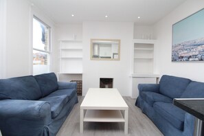 Una sala de estar moderna con dos sofás azules, una mesa de centro blanca y estanterías empotradas blancas.