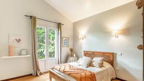 Ein Schlafzimmer mit einem Holzbett, einem Fenster mit Vorhängen, einem Nachttisch mit Lampe und Wandleuchten.