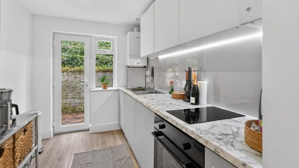 A modern kitchen with white cabinets, a black stove, and a marble countertop. - Madeira 2BR Garden Retreat in Bromley with Street Parking (Greater London)