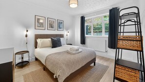 A bedroom with a bed, bedside tables, a window with curtains, a wall-mounted light, and framed pictures. - Madeira 2BR Garden Retreat in Bromley with Street Parking (Greater London)