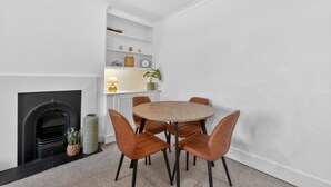 A dining area with a round table, six chairs, a fireplace, and a white wall with shelves. - Madeira 2BR Garden Retreat in Bromley with Street Parking (Greater London)