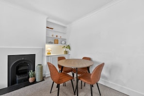 A dining area with a round table, six chairs, a fireplace, and a white wall with shelves.