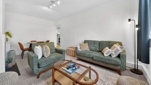 A living room with a sofa, armchair, coffee table, and a dining area with chairs and a table. - Madeira 2BR Garden Retreat in Bromley with Street Parking (Greater London)