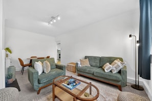 A living room with a sofa, armchair, coffee table, and a dining area with chairs and a table.