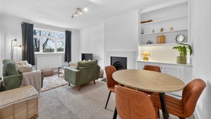 A modern living room with a sofa, armchairs, a dining table, and a fireplace. - Madeira 2BR Garden Retreat in Bromley with Street Parking (Greater London)