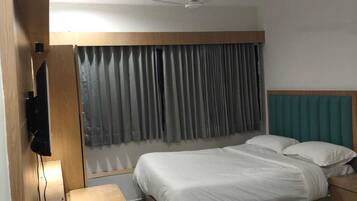 Habitación de hotel con dos camas, televisión, ventilador de techo y ventana con cortinas.
