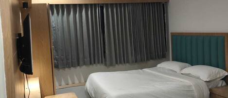 A hotel room with two beds, a TV, a ceiling fan, and a window with curtains.