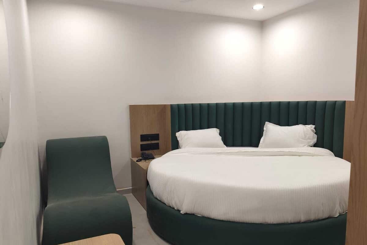 A modern hotel room with a round bed, a green upholstered chair, a wooden nightstand, and a small table.