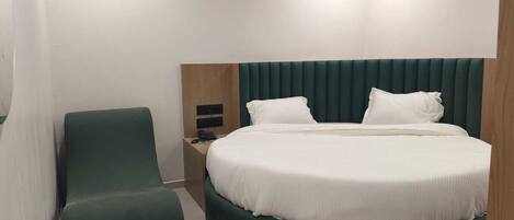 Ein modernes Hotelzimmer mit einem runden Bett, einem grünen Polsterstuhl, einem Holznachttisch und einem kleinen Tisch.