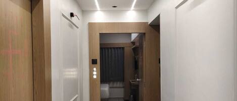 Un couloir d’hôtel avec une porte en bois sur la gauche, une plaque portant le numéro « 108 », et une chambre visible à travers l’ouverture de la porte.