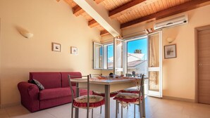 Una stanza accogliente con un divano rosso, un tavolo da pranzo con sedie e ampie finestre che offrono vista all'esterno.