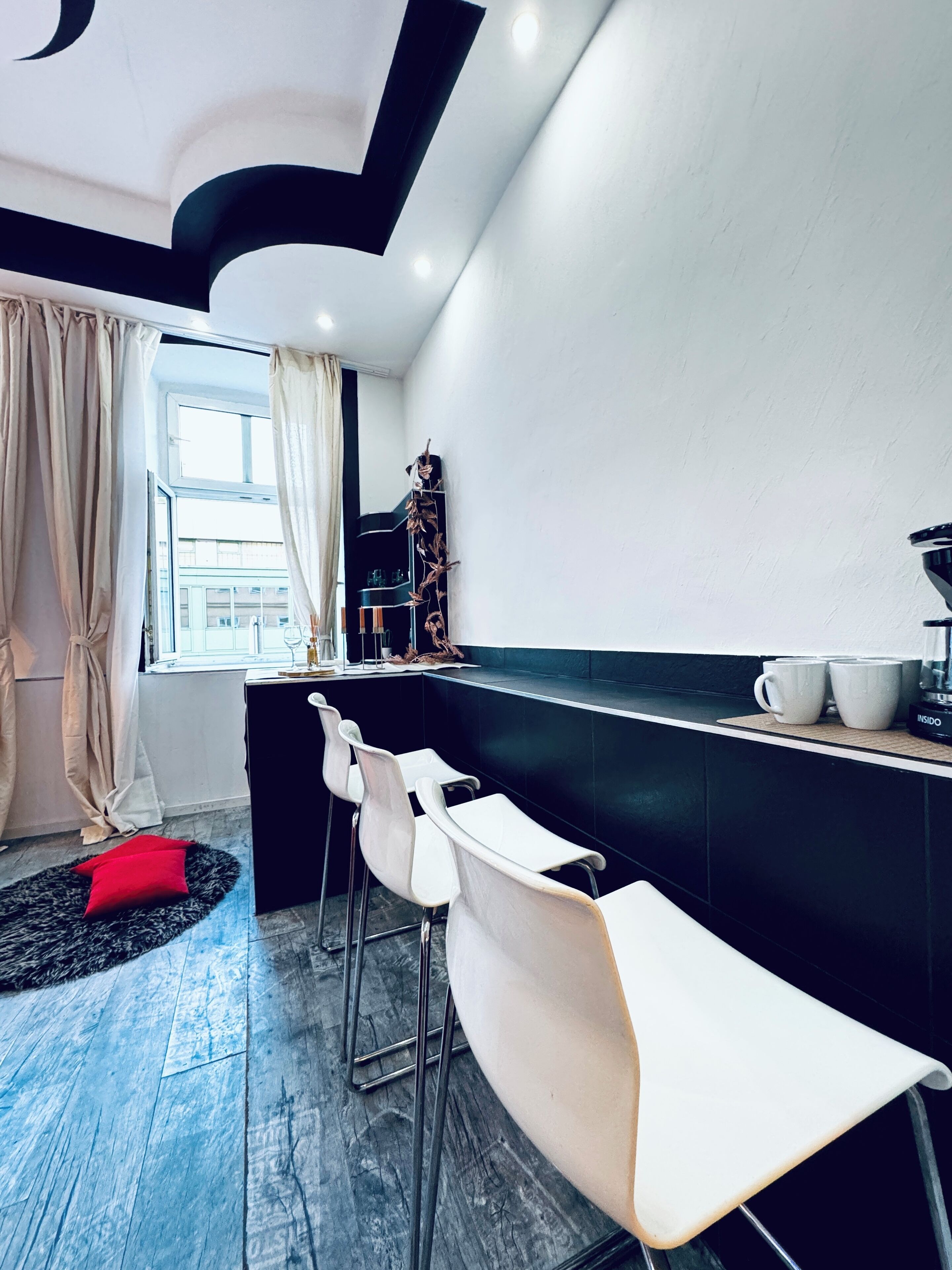Une cuisine moderne avec un coin bar, des tabourets de bar blancs et un plan de travail noir.