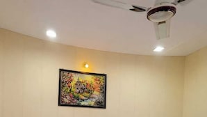 A hotel room with a bed, a ceiling fan, a wall-mounted light, and a framed picture. - Hotel Laxman Grand (Rishikesh)