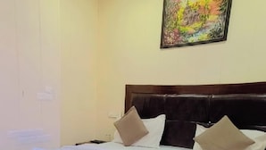 A hotel room with a bed, a chair, and a painting on the wall. - Hotel Laxman Grand (Rishikesh)