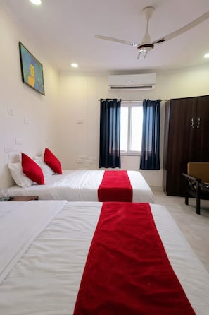 A hotel room with two beds, red and white bedding, a ceiling fan, an air conditioning unit, and a window with curtains. - Hotel Laxman Grand (Rishikesh)