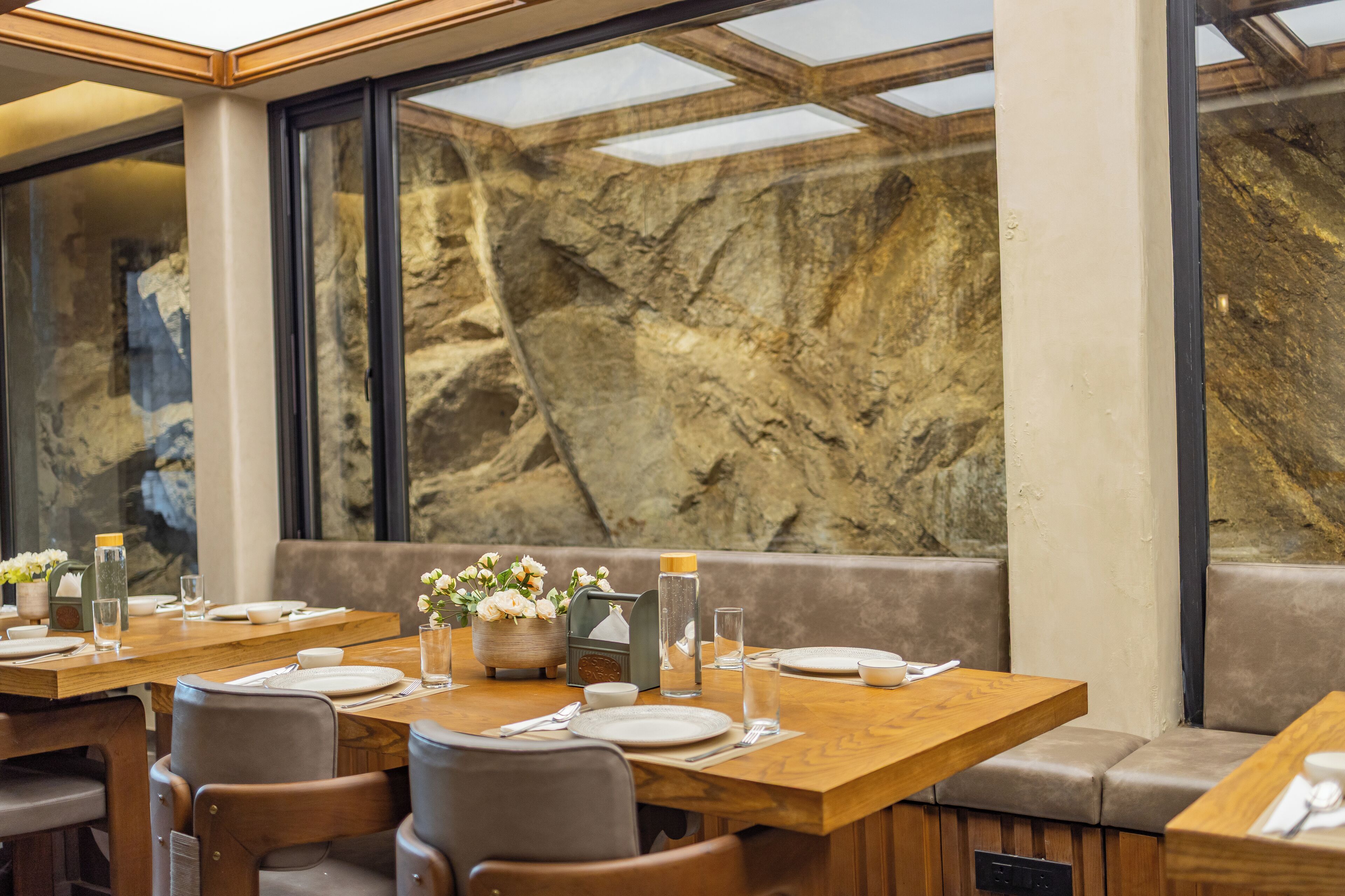 Ein Restaurant mit Holztischen, gepolsterten Sitzplätzen, großen Fenstern und einer Wand aus Stein.
