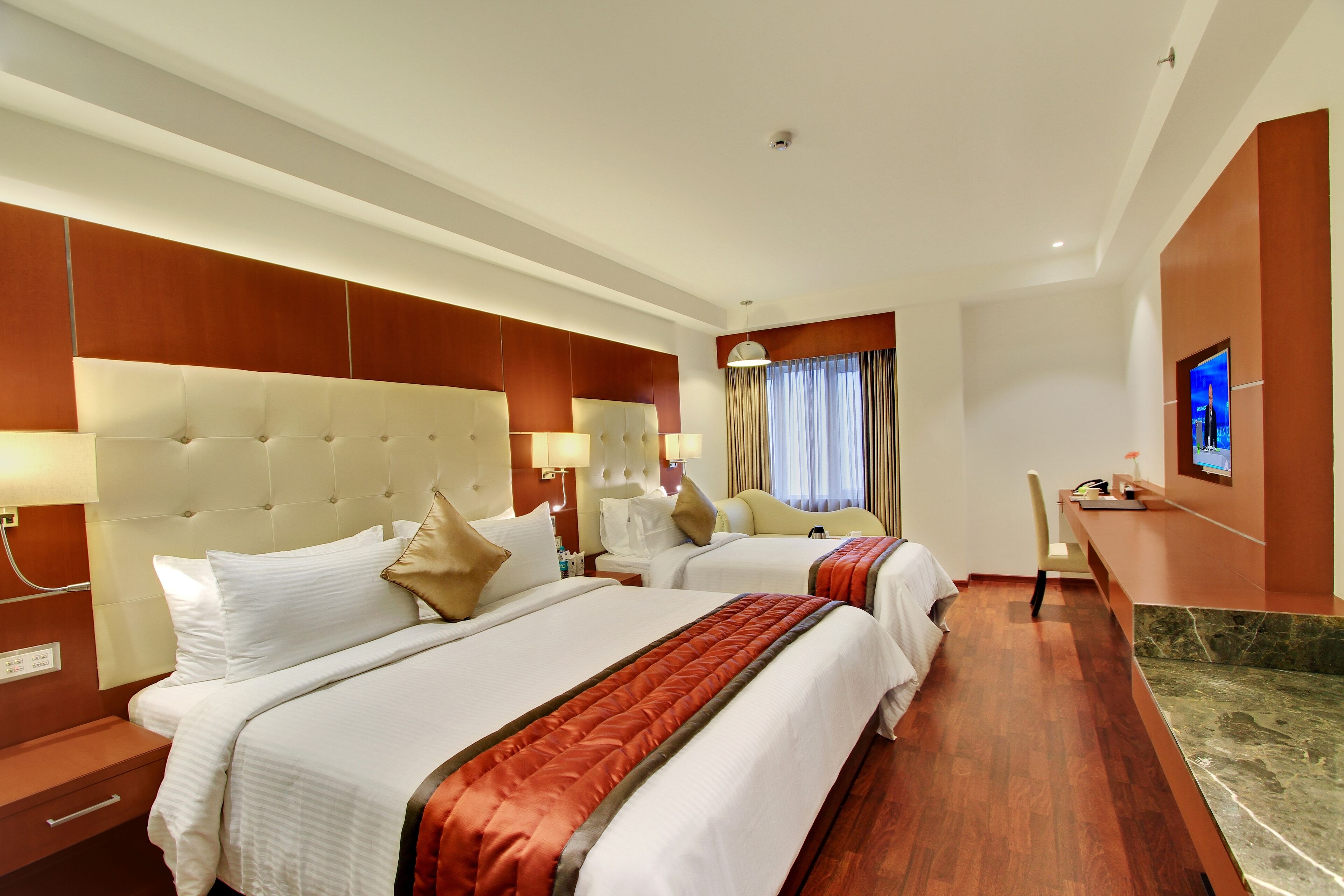 A hotel room with two beds, a desk, a TV, and a bathroom.