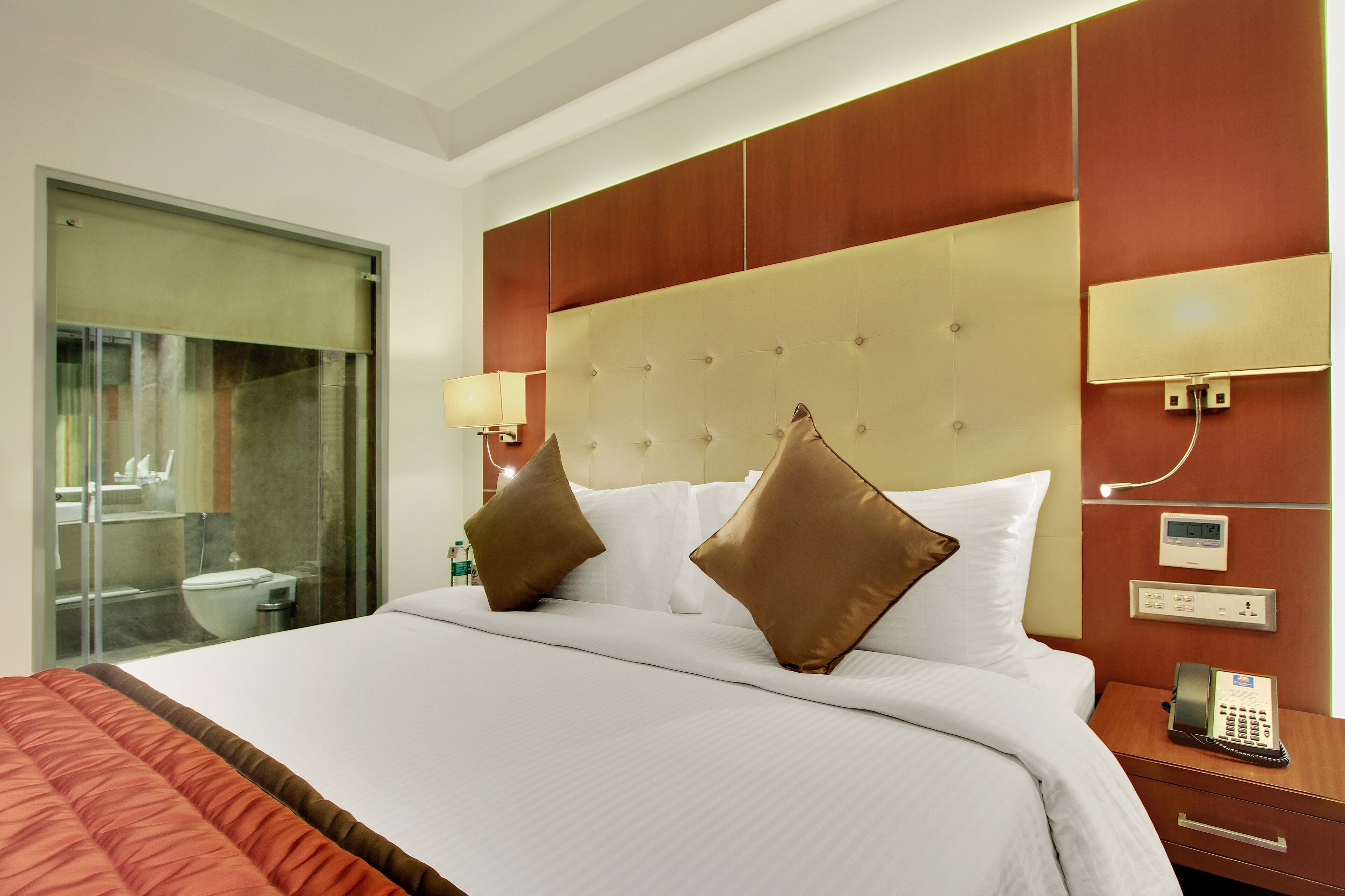 A hotel room with a large bed, a bedside telephone, and a glass-enclosed bathroom.